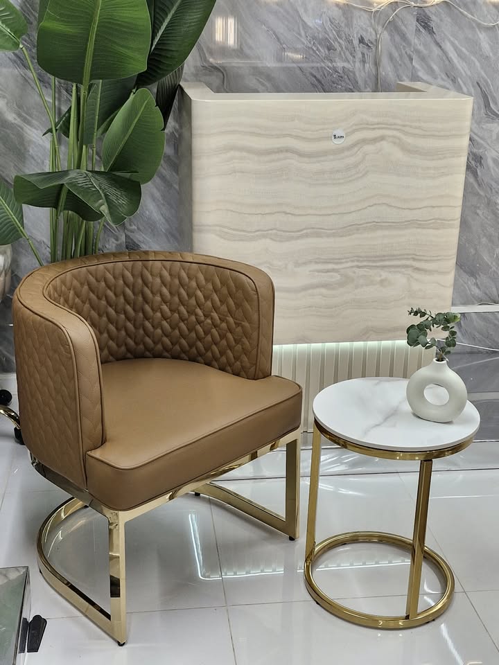 Brown quilted chair with gold legs in a room with marble walls and a small table.