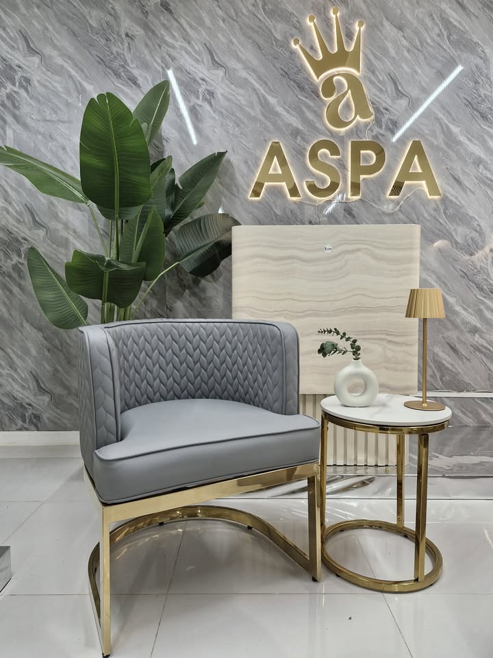 Gray chair with gold legs in a room with a marble wall and 'ASPA' logo.