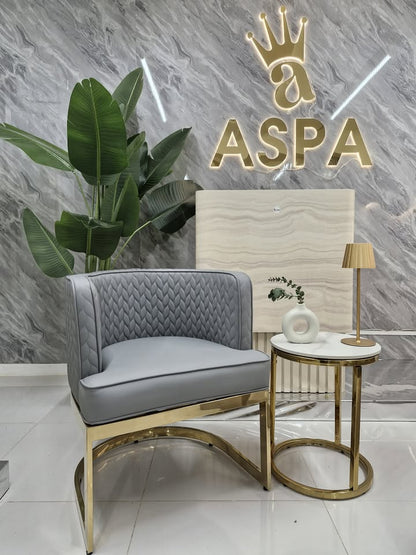 Gray chair with gold legs in a room with a marble wall and 'ASPA' logo.