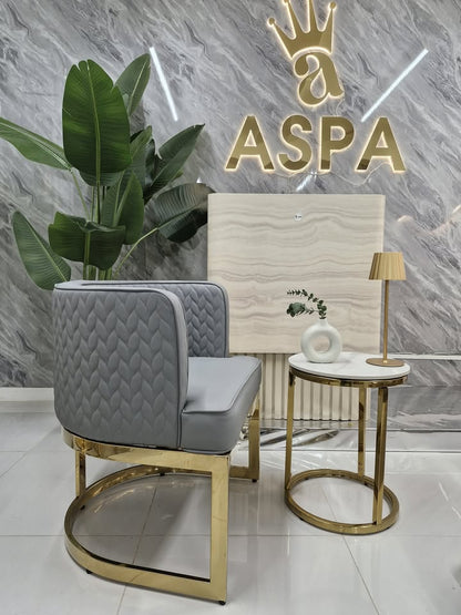Modern interior design with gray upholstered chair, gold legs, and marble wall with 'ASPA' logo.