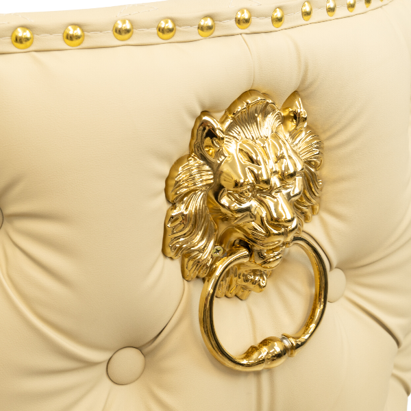 Close-up of a gold lion head knocker on a cream tufted leather chair with gold nailhead trim