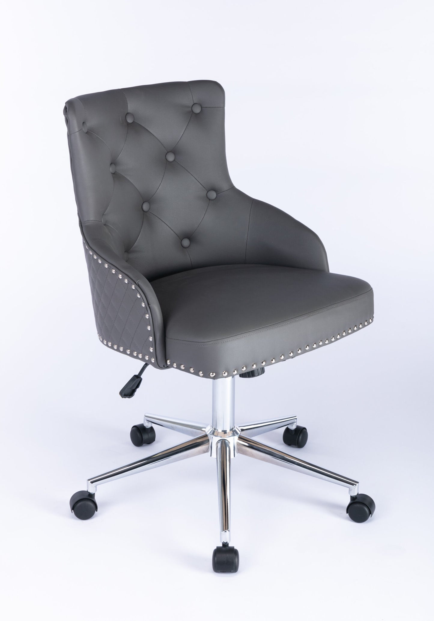 Three-quarter front view of a grey upholstered swivel office chair with button-tufted backrest, curved padded arms, nailhead trim around the seat edge, quilted side panels, and a chrome five-star base with castors and height adjustment lever.