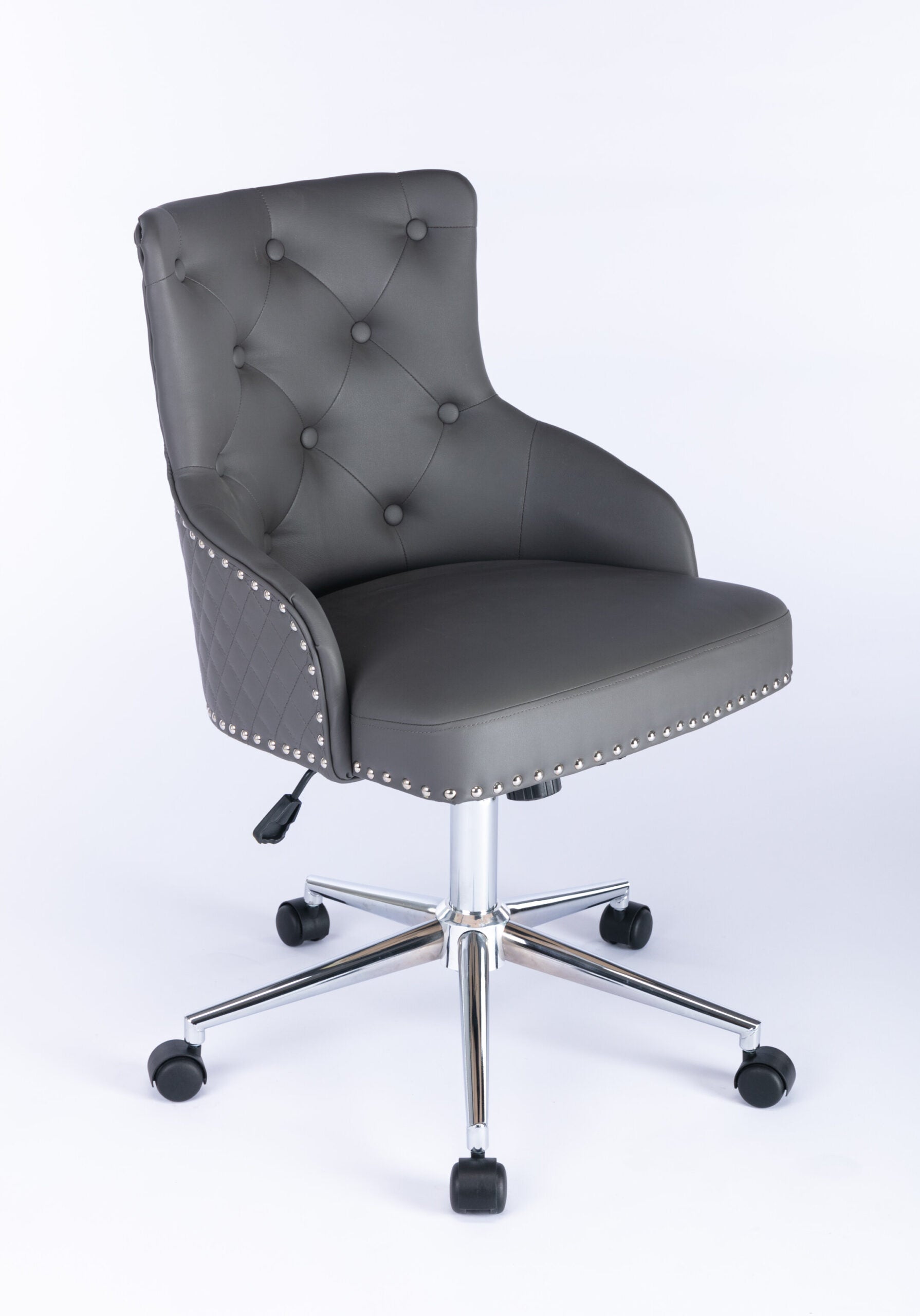 Three-quarter front view of a grey upholstered swivel office chair with button-tufted backrest, curved padded arms, nailhead trim around the seat edge, quilted side panels, and a chrome five-star base with castors and height adjustment lever.